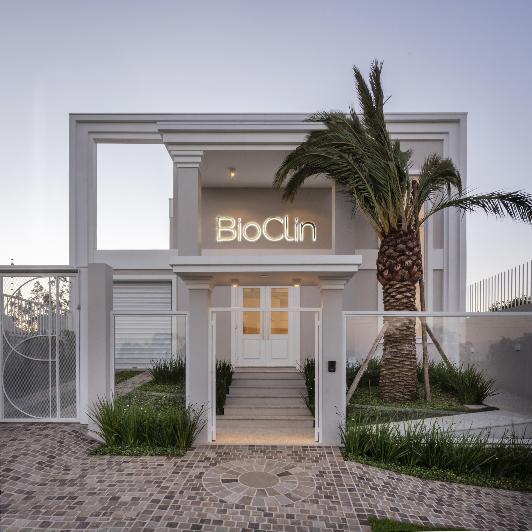 Fachada da Bioclin ao anoitecer, com palmeira e letreiro iluminado